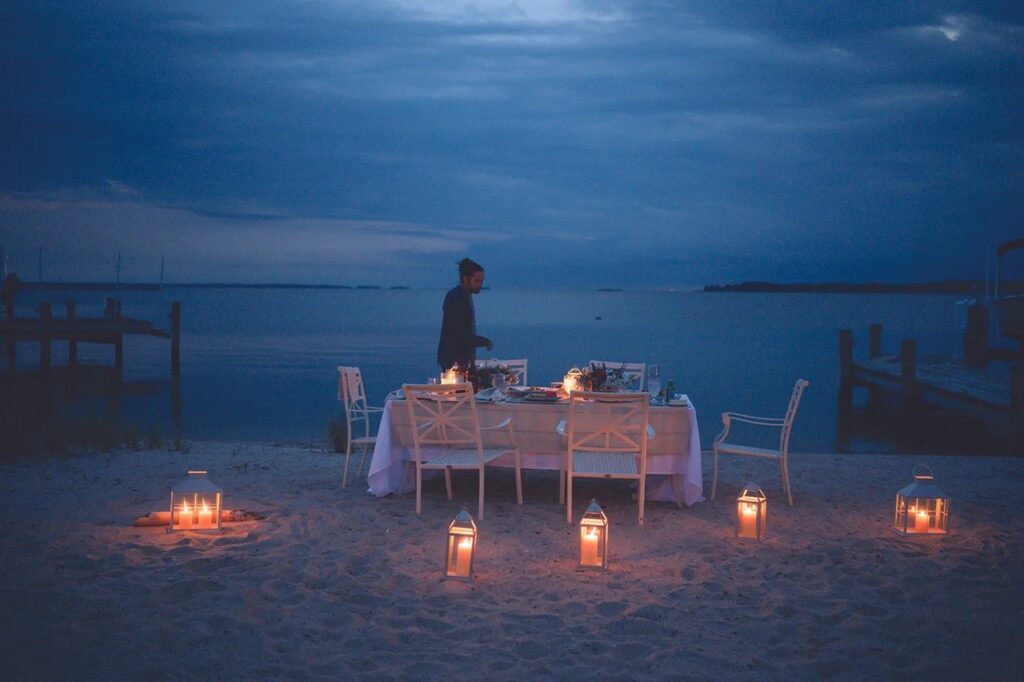 A man walks past a dining table on the Chesapeake Bay with candles.