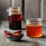 A jar of easy homemade hot honey sits beside a jar of chili crisp and a small bowl of red chiles.