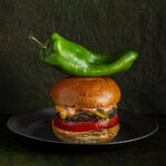 A cheeseburger sits on a plate with a large green chile sitting on top of it.