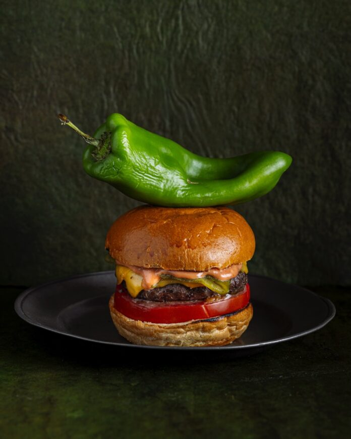 A cheeseburger sits on a plate with a large green chile sitting on top of it.