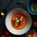 An above shot of a bowl of heirloom tomato soup in a white bowl with a thin blue line around the rim.