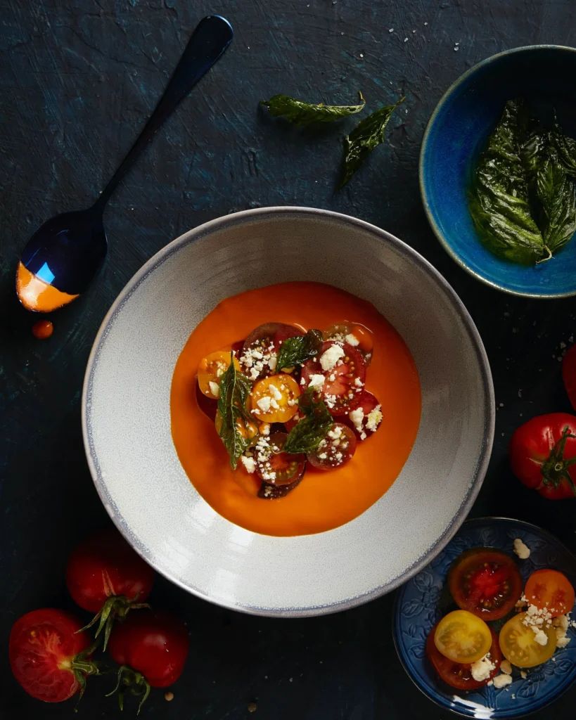 An above shot of a bowl of heirloom tomato soup in a white bowl with a thin blue line around the rim.