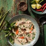A grey bowl full of a Martha Stewart Slow Cooker Tom Kha Gai with leafy greens garnish sits on a green picnic table.