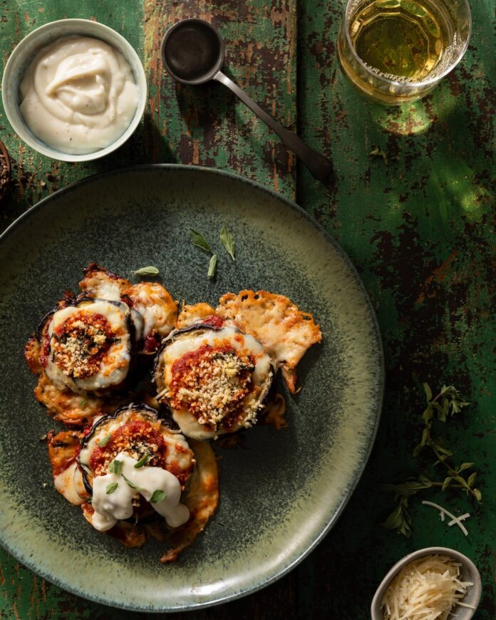 A green plate with Martha Stewart-Inspired Stacked Eggplant Parmesan individually on a plate with a beschamel sauce off to the side.