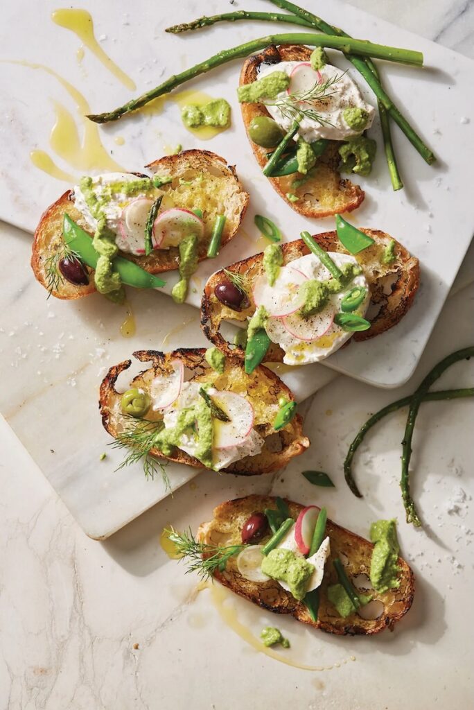 A variety of Pesto-Burrata Crostinis with spears of asparagus beside them.