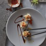 A plate of Pork and Shrimp Shumai dumplings hold with chopsticks with a sauce drizzled over top.