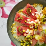 An above shot of a bowl filled with brightly colored fruit, making up a watermelon steak salad.