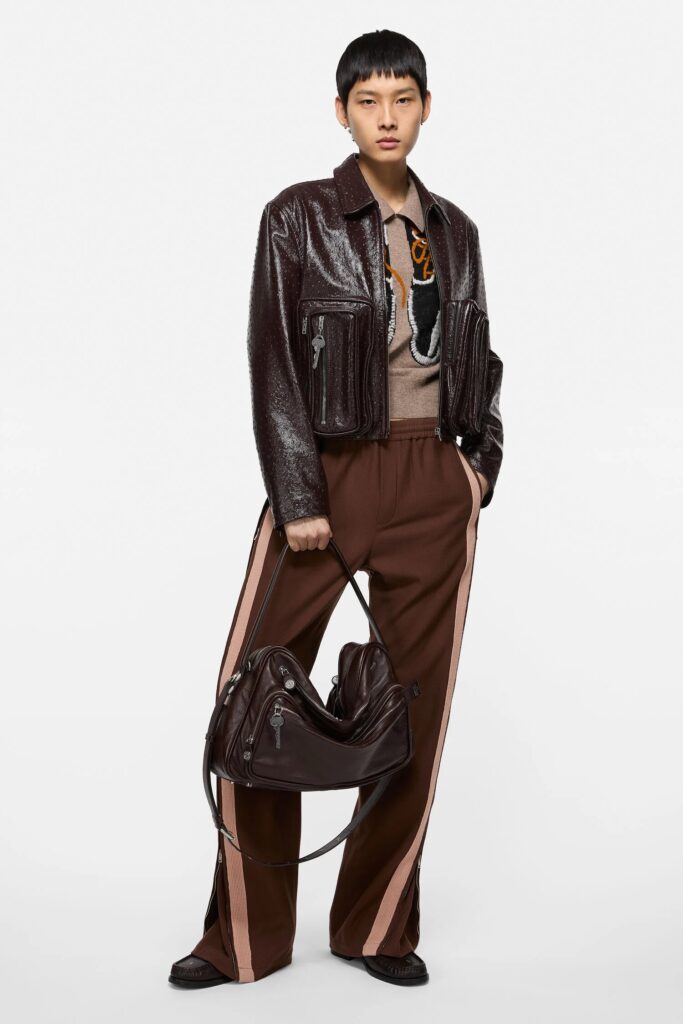 A person in an all brown layered outfit with a jacket and purse.