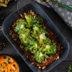 A plate of grilled broccoli with romesco sauce, topped with parsley and chopped nuts, with a small bowl of capers.
