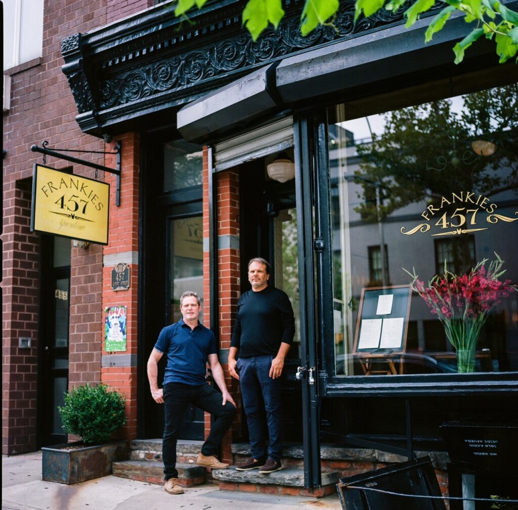 Two chefs stand outside of a restaurant.