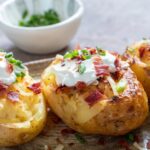 A platter of three loaded baked potatoes topped with recipes like leftover chili, sour cream, bacon bits, and chopped chives.