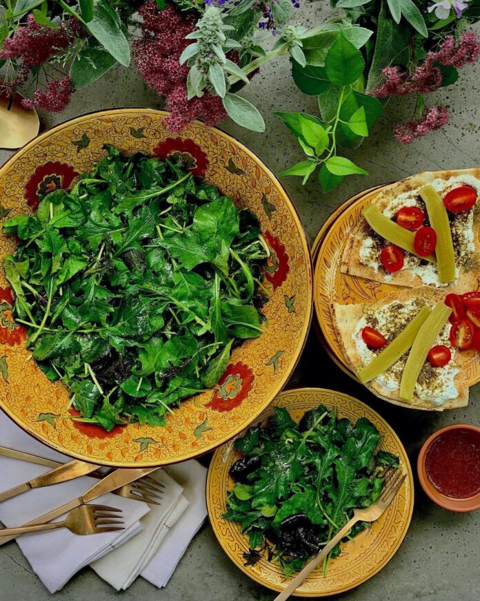 A large bowl of fresh, leafy green salad with a smaller serving on a plate with pita bread