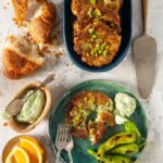 A platter of golden brown kohlrabi and leek fritters, with a bowl of yogurt sauce, and a croissant.