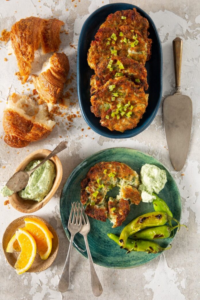 A platter of golden brown kohlrabi and leek fritters, with a bowl of yogurt sauce, and a croissant.