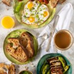 A Spanish breakfast with fried eggs and chorizo, grilled halloumi cheese with green peppers, and bowls of zhoug sauce and orange juice, all served with toasted bread.