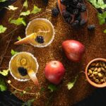 A pair of pear cider and gin bellinis in sugar-rimmed glasses, garnished with blackberries and pear slices, on a textured placemat.