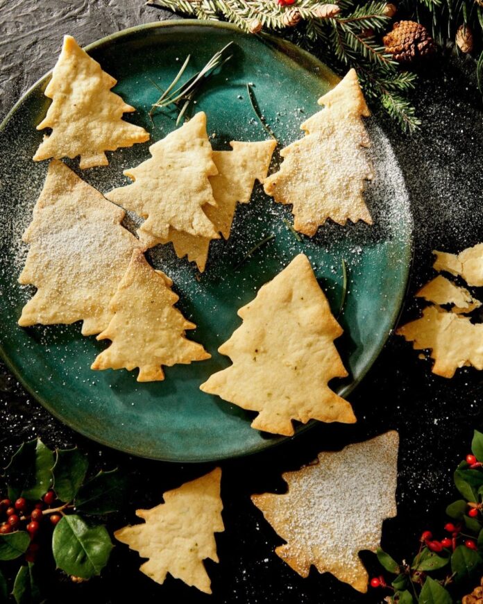A dark green plate filled with Christmas tree-shaped shortbread cookies, some dusted with powdered sugar.