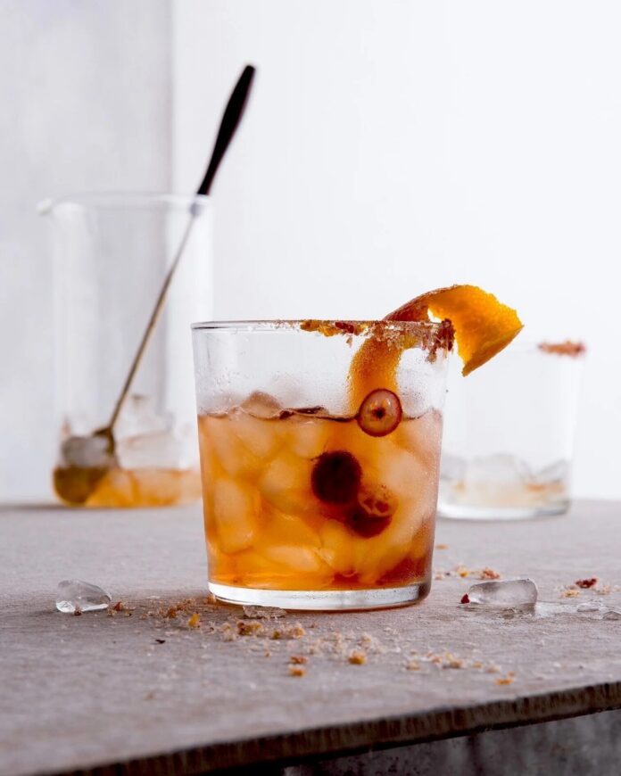 Rye Cranhattan A glass of Rye Cranhattan on a table with ice, garnished with a cranberry and an orange peel.