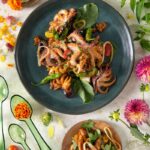 Sauteed Octopus with Criolla Sauce served on a dark green plate with a side dish.