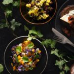 Roasted cauliflower with ginger and turmeric on a black plate, drizzled with a creamy sauce and garnished with fresh greens.