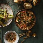 A green picnic table with a Caesar salad, garlic knots, and beans and greens bowl on top.