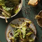 Two plates of caesar salad with seasonings all over on a green table.