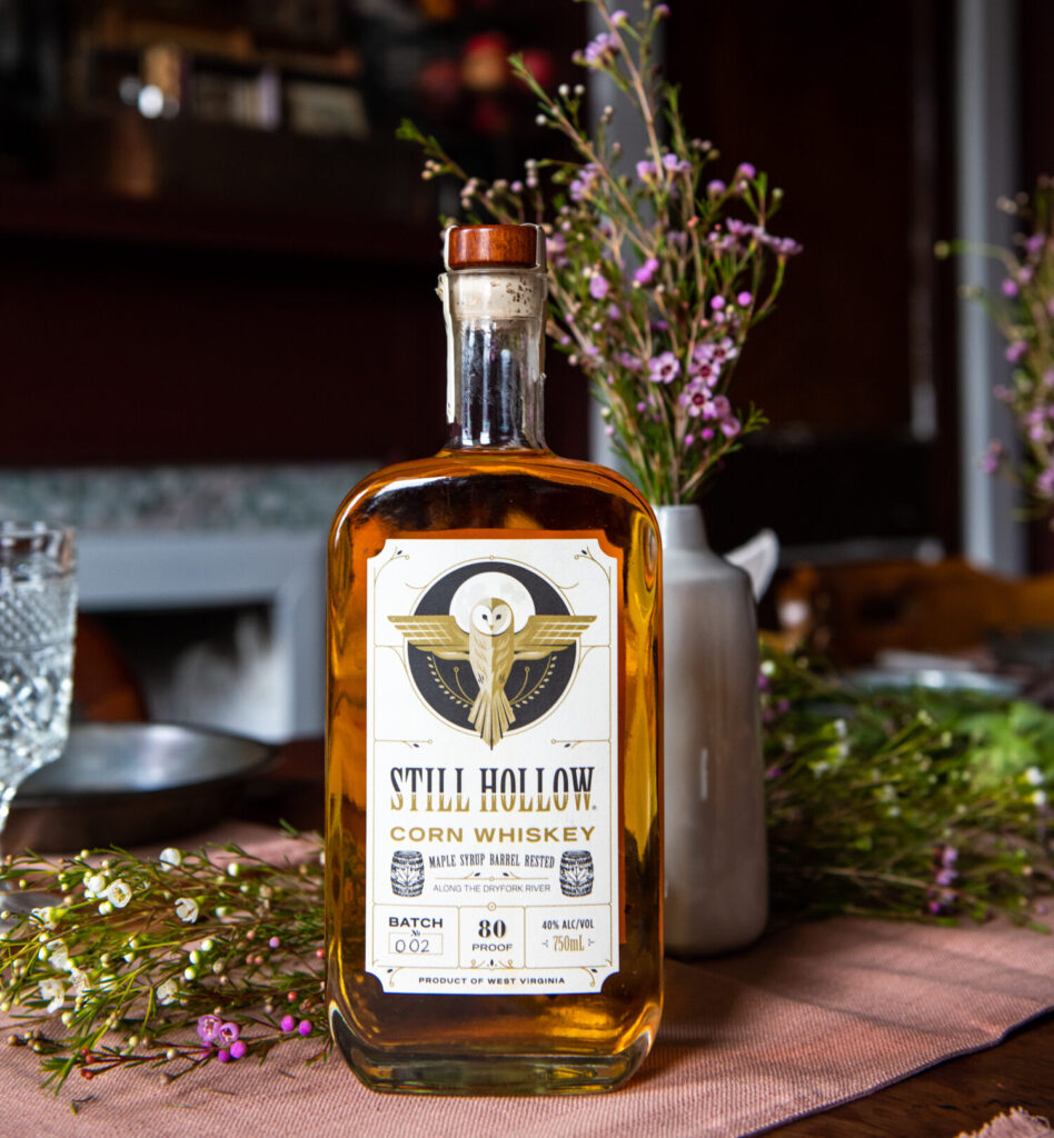 An amber bottle of corn whiskey on a picnic table with flowers.