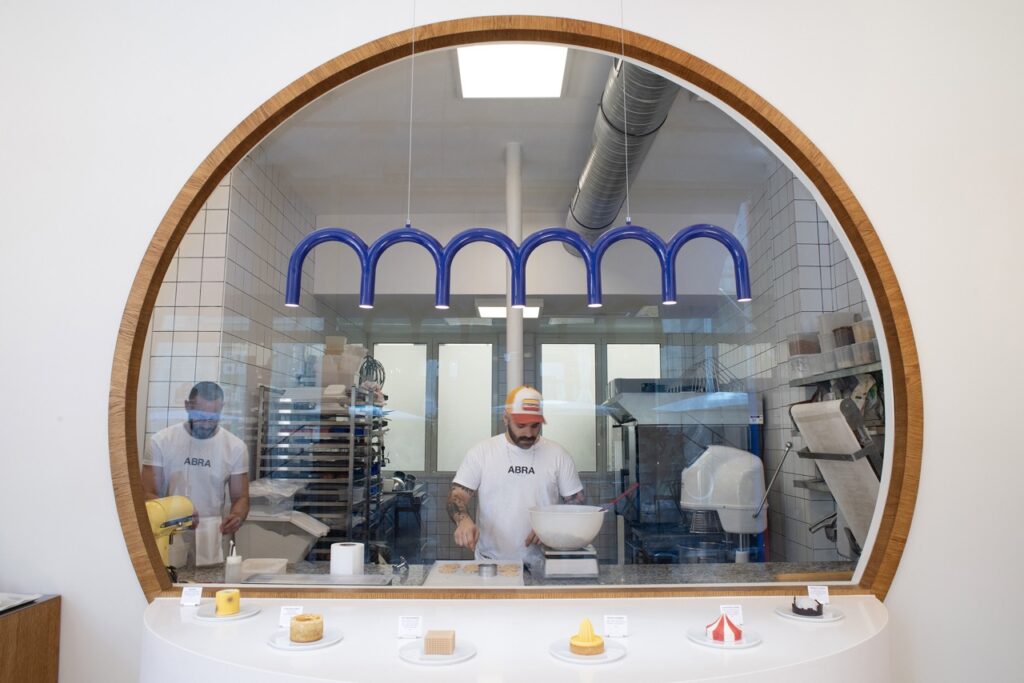 A pastry maker in Paris works behind glass as various pastries sit in front of his station.