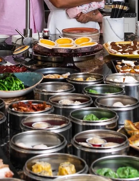 Egg Tart Various silver trays of dumplings sit in front of a tray of egg tarts.