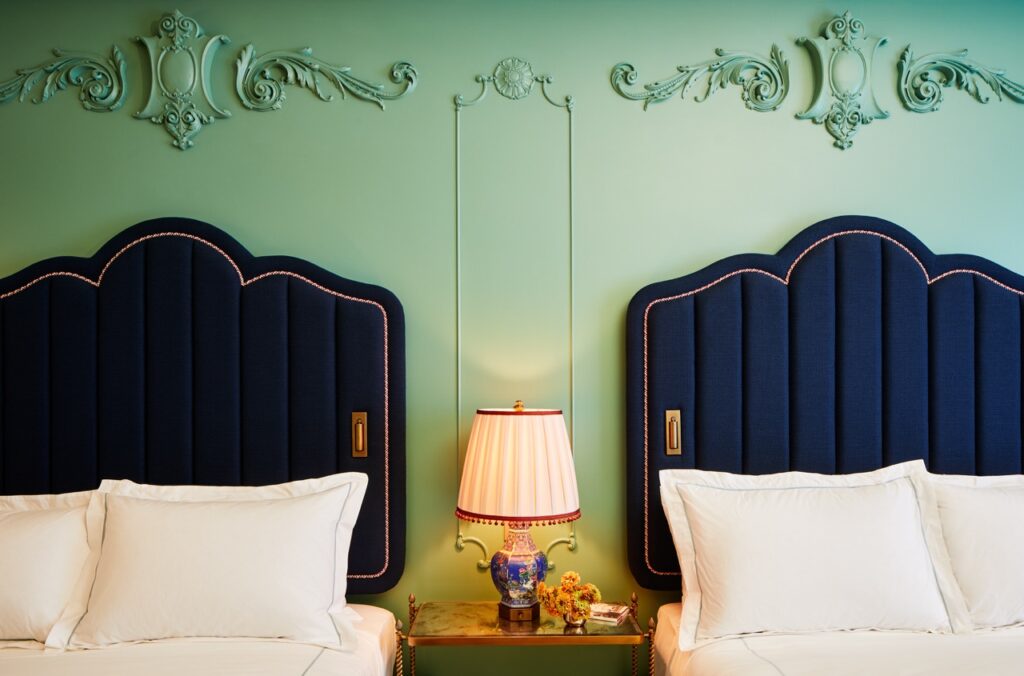 A lamp sits between two bed headboards against a mint green wall.