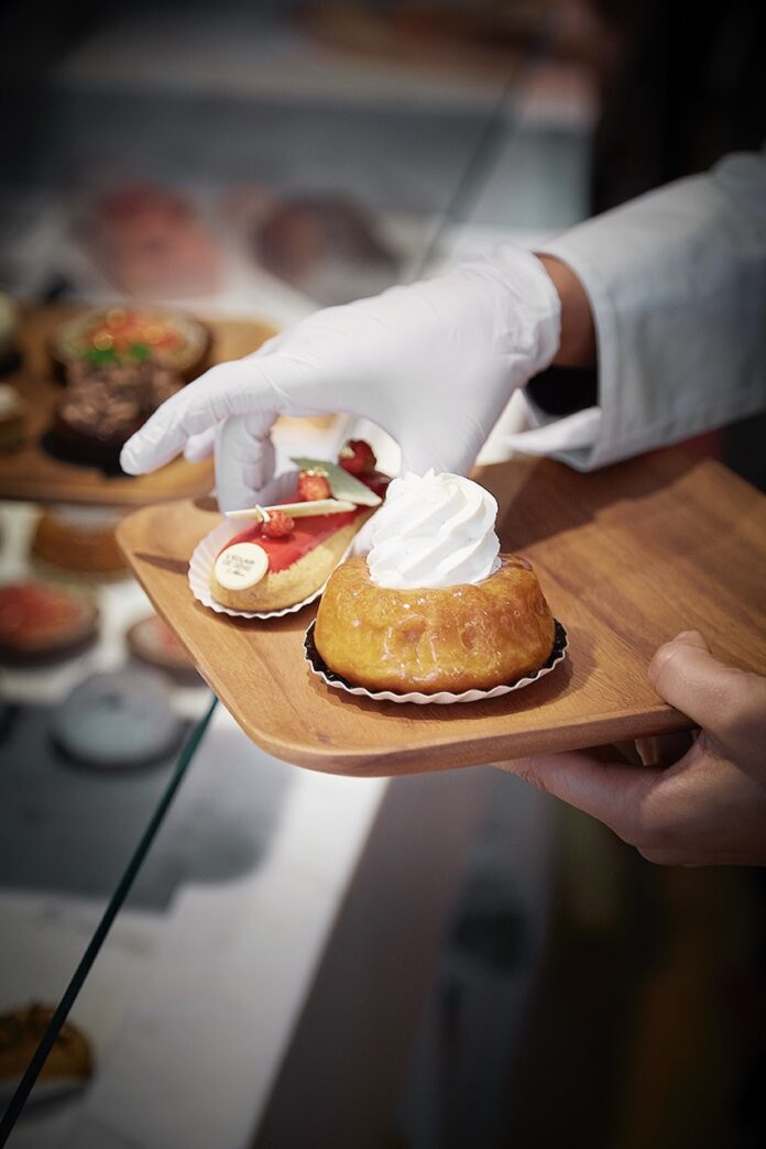 A baker grabs an eclair and small cake from the bakery case.