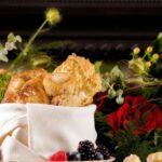 A basket of golden Glendorn Drop Biscuits and fresh berries on a white plate, surrounded by red roses and green foliage.