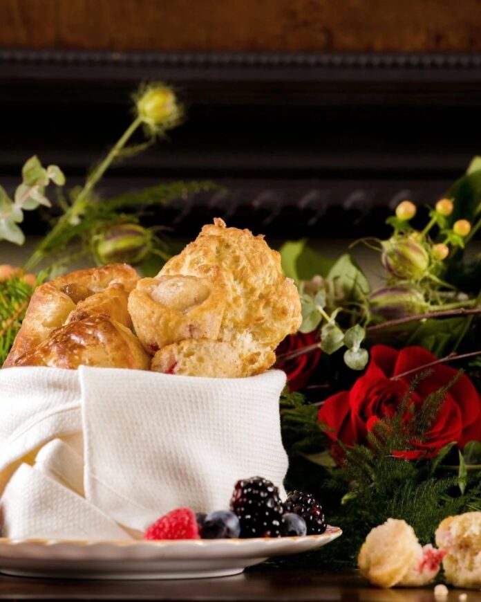 A basket of golden Glendorn Drop Biscuits and fresh berries on a white plate, surrounded by red roses and green foliage.