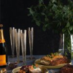 two yellow plates with slices of layered meatloaf, accompanied by flutes of champagne and a glass bottle on a table.