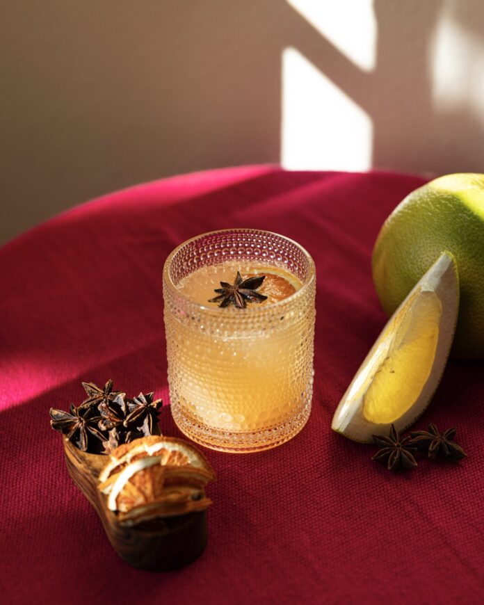 A chai masala good luck mimosa with grapefruit juice sits on a red table top with a star anise garnish in the glass and citrus slices nearby.
