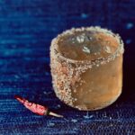 A rocks glass with The Boss rum cocktail in it with a salt and sugar rim. It sits on a blue surface beside a chile pepper.