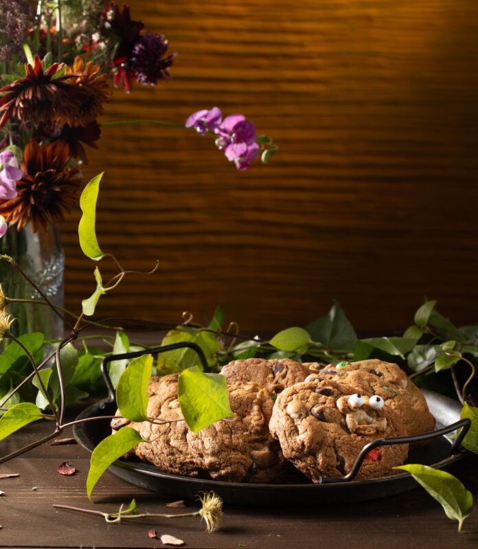 A plate full of candy cookies with googly eyes candies on them amongst flowers and vines.