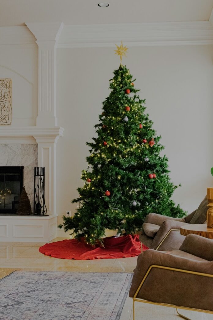 A Christmas tree fully decorated in a white living room with a gold star on top.