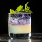 A Wicked: For Good cocktail sits on a black table with mint leaves for garnish.