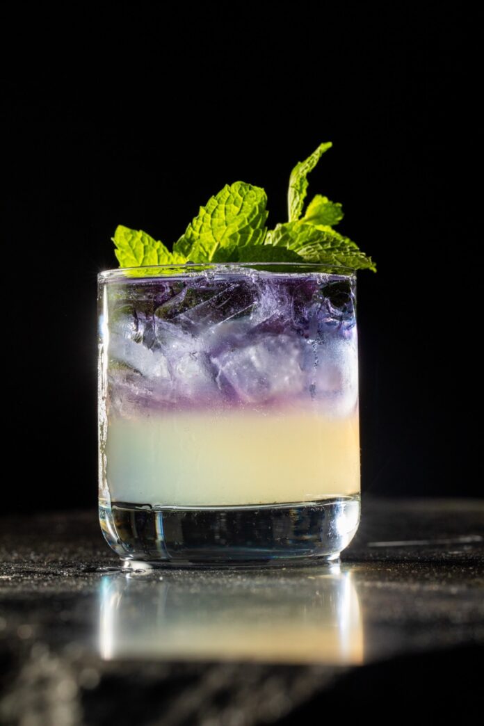 A Wicked: For Good cocktail sits on a black table with mint leaves for garnish.