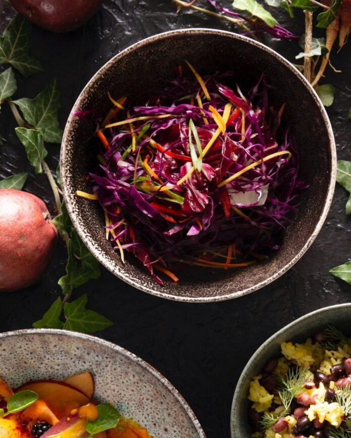 A bowl filled with vibrant purple and yellow julienned red cabbage, radicchio, and peppers, garnished with scallions.