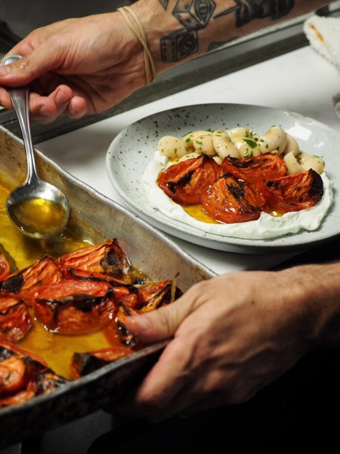 A chef in Miami scoops tomatoes onto a plate with potatoes.