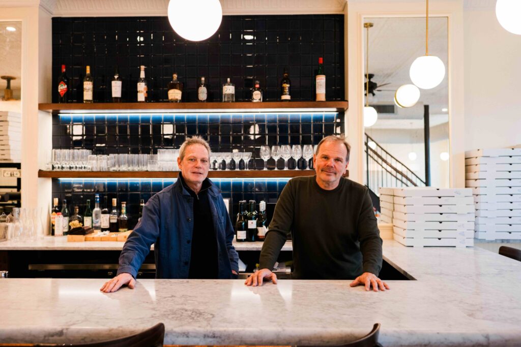Two men stand at a marble white pizza counter.