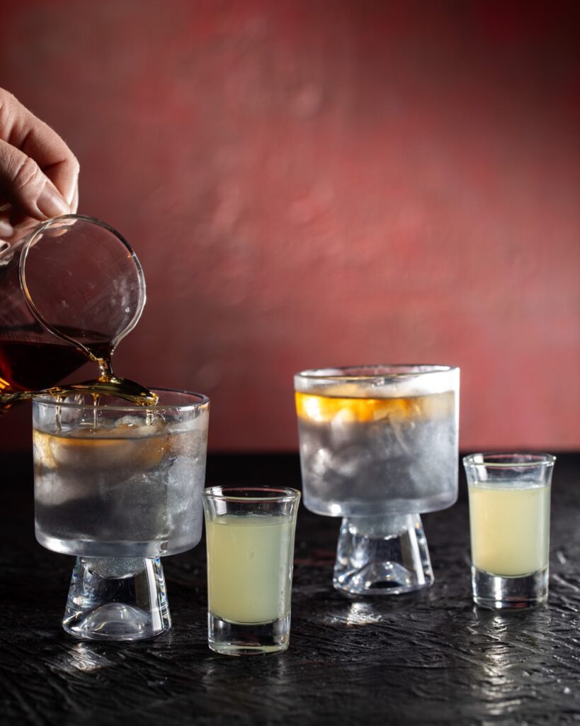 Someone spoons rum over a cocktail glass.