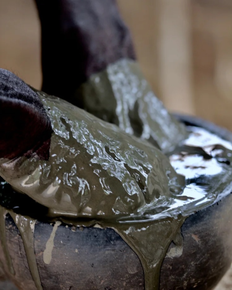 Dark clay bowl filled with thick, iron-rich green-brown mud from the Niger River, which is fermented for a year to create a dye for bògòlanfini mudcloth.