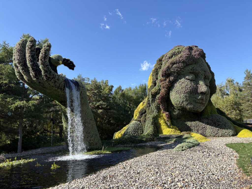 A woman statue in a pond with water falling over her hand.