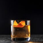 A short glass with a clear old fashioned for the release of Now You See Me Now You Don't with an orange peel twist as a garnish.