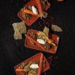 Three orange rectangular plates with pickled baby carrots, smoked labneh, and lentils.