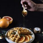 A stack of sweet potato waffles with citrus slices and a drizzle of honey over top.