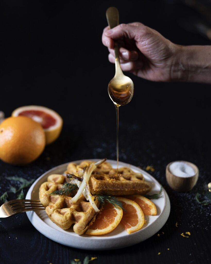 A stack of sweet potato waffles with citrus slices and a drizzle of honey over top.